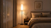 A serene bedroom scene with a made bed, a lamp on a nightstand, and a window providing a view outside