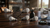 A living room table with scattered light bulbs, a geometric sculpture, and a small plant vase. Stone fireplace and large window in the background, creating a calm, cozy ambiance.